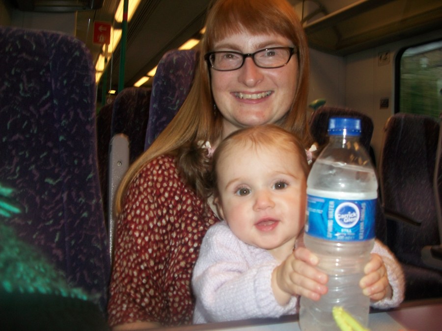 Image of a woman with long ginger hair and glasses, holding a baby girl on her knee as they journey by train. #MummyMonday Family Day Trip on the Train from Manchester to York at SpookyMrsGreen.com mindful parenting and modern pagan lifestyle blog.