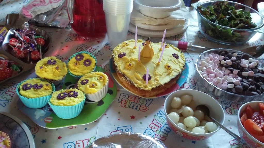 Photo of a Disney Beauty and the Beast birthday cake, yellow cupcakes with flower frosting, marshmallow and chocolate buttons, party food buffet. #MummyMonday Planning a Birthday Party for my Daughter SpookyMrsGreen.com mindful parenting and modern pagan lifestyle blog.