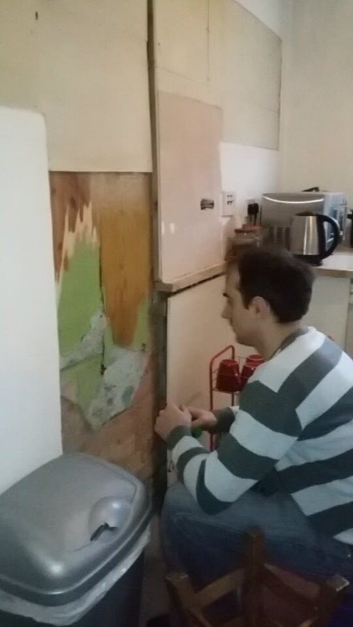 Image of a man crouching in a small kitchen, studying the walls during renovation, in a Victorian terraced house in UK. My Kitchen Renovation: Assessing the Damage at SpookyMrsGreen.com mindful parenting and modern pagan lifestyle blog.