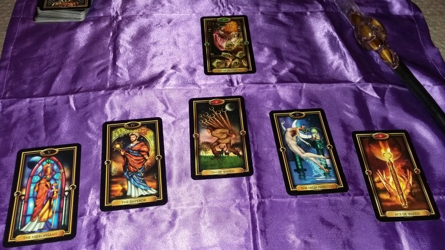 Photo of Gilded Tarot cards on a purple cloth with a clear quartz and Tiger's Eye crystal wand belonging to Catherine Green. Ostara Tarot card reading with Gilded Tarot cards performed by professional Tarot reader Catherine Green of SpookyMrsGreen.com pagan lifestyle blog.