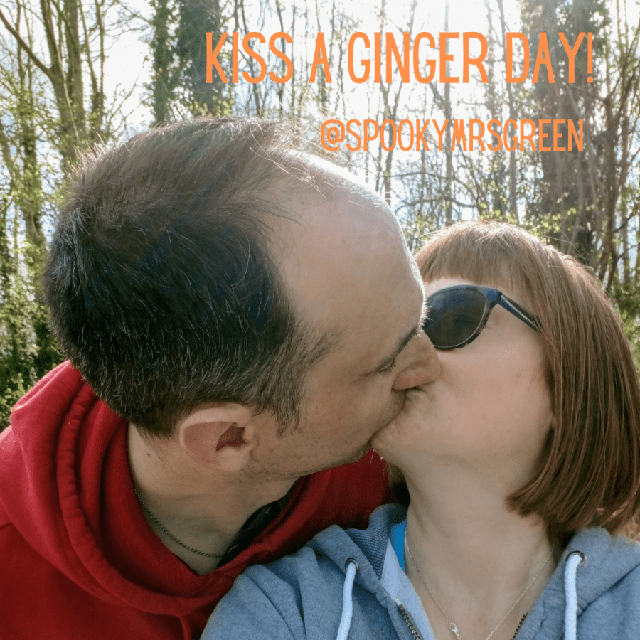 Image of LGBT fantasy book writer Catherine Green kissing her husband as they stand in a forest on a sunny day. Image of a man and woman kissing passionately. Text reads, "Kiss a Ginger Day @SpookyMrsGreen." Kiss a ginger day at SpookyMrsGreen.com mindful parenting and modern pagan lifestyle blog.