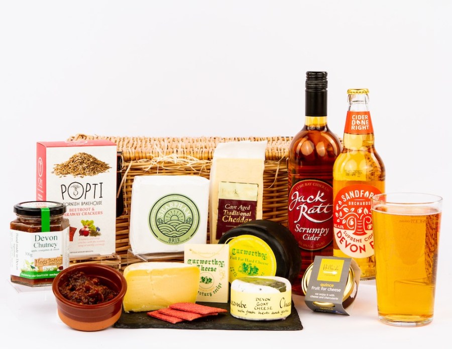 Photo of a wicker hamper, bottles of ale and cider, glass of beer, cheese, preserves and biscuits. Devon Hampers Father's Day Gift Ideas