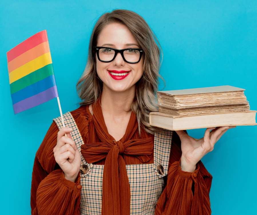 Image of a librarian holding LGBT fantasy books in one hand and a Pride flag in her other hand. Article for Pride Month LGBTQ+ fiction.