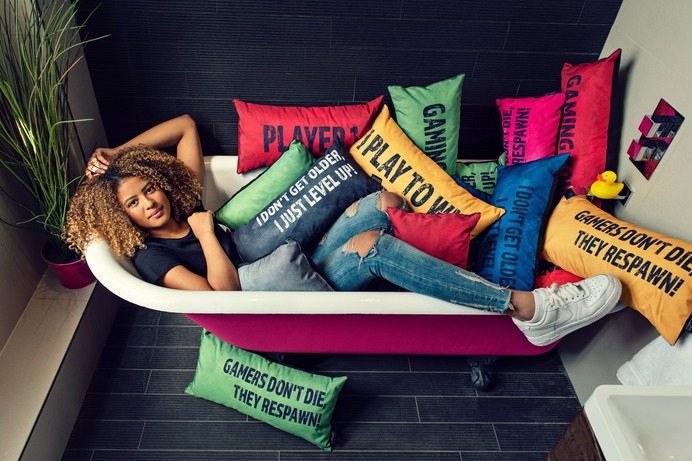 Image of a woman lying in a bath beneath a pile of gaming cushions with gaming slogans printed on them. Game Over Gaming Bean Bags and Chairs affiliated with SpookyMrsGreen.com mindful parenting and modern pagan lifestyle blog.