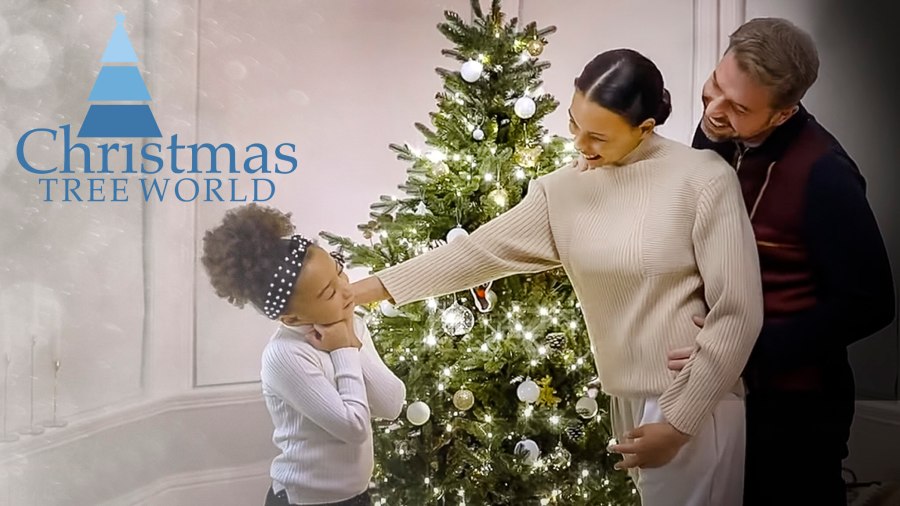 Text reads, "Christmas Tree World." Cosy image of a Christmas tree with warm lights and a young family standing around the tree smiling and having fun together. Christmas Tree World affiliated with SpookyMrsGreen.com mindful parenting and modern pagan lifestyle blog.