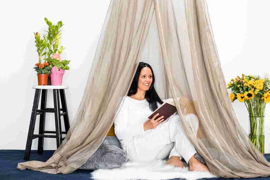 Image of a woman sitting underneath a Shield Your Body SYB Serenity Canopy reading a book and smiling. Shield Your Body affiliated with SpookyMrsGreen.com mindful parenting and modern pagan lifestyle blog.