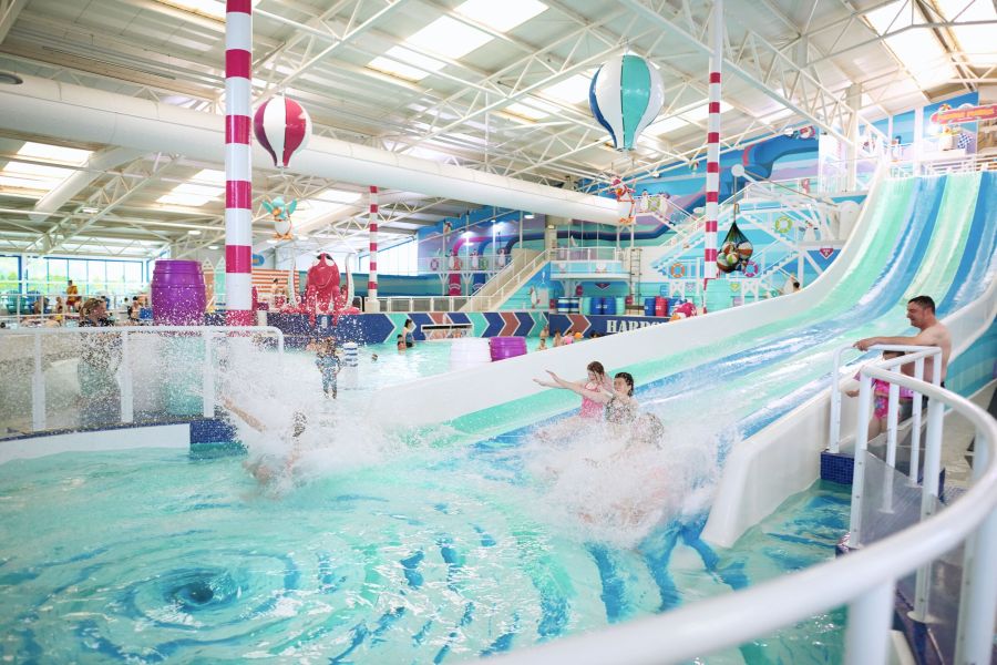 Image of a colourful indoor water park with families having fun in the pool and sliding down water slides. May Half Term breaks from 329GBP at Haven affiliated with SpookyMrsGreen.com mindful parenting and modern pagan lifestyle blog.