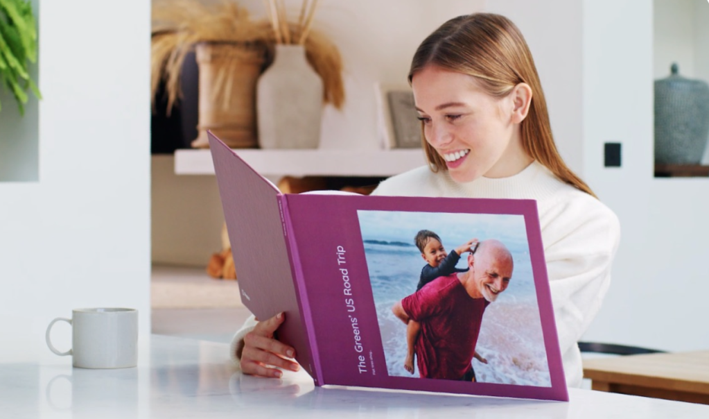Image of a girl looking at photos in a photo book and smiling. Fantastic June Savings at Popsa affiliated with SpookyMrsGreen.com mindful parenting and modern pagan lifestyle blog.