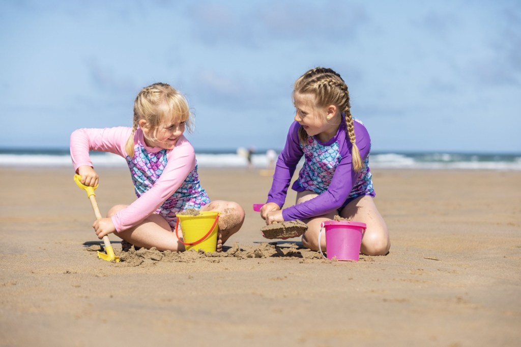 Colourful image of two girls digging in the sand and building sandcastles on a beach. Image provided by Haven holidays affiliated with SpookyMrsGreen.com mindful parenting and modern pagan lifestyle blog.