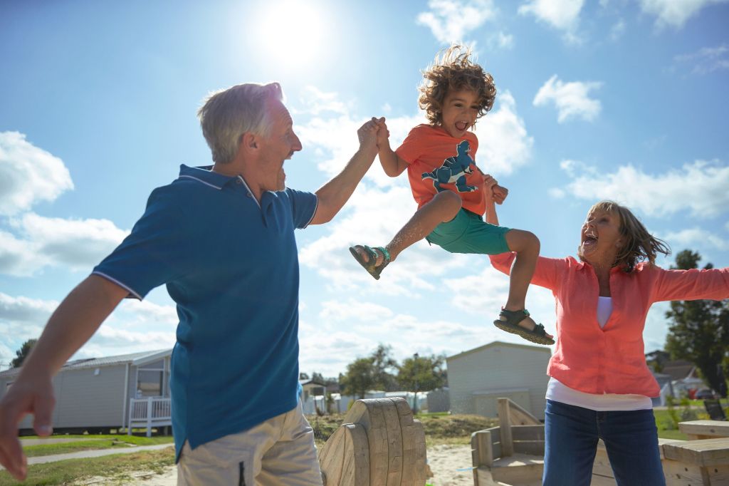 Image of a mum and dad lifting their child up in the air enjoying their holiday with caravans in the background. Last minute UK breaks and caravan holiday deals with Haven affiliated with SpookyMrsGreen.com mindful parenting and modern pagan lifestyle blog.